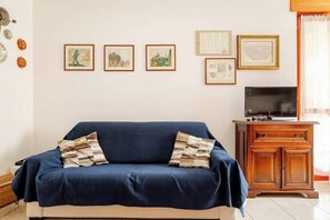 A room with a blue sofa, a wooden cabinet, and framed artwork on the wall. - Casa Emy da Teresina – Relax in a Green Setting Just a Stone's Throw from Alba (Reala)