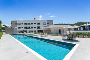 Een modern hotel met een zwembad, terras en uitzicht op een heuvel.