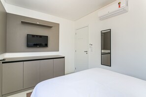 Quarto de hotel moderno com cama, televisão fixada na parede, guarda-roupa, porta com tranca de segurança e espelho.