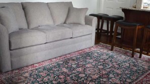 A living room with a sofa, a patterned rug, and a kitchen area with stools.