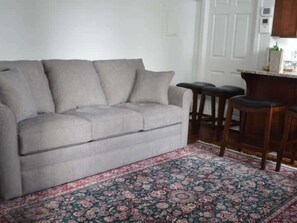 Una sala de estar con un sofá, un tapete estampado y una zona de cocina con taburetes.