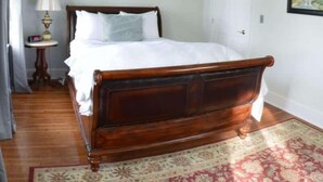 A neatly made bed with a wooden headboard in a room with a small side table and a lamp.