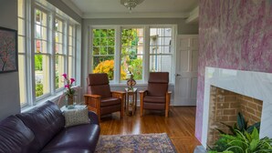 A living room with a leather sofa, two chairs, a patterned rug, a fireplace, and large windows with a view of greenery.