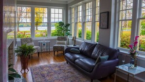 A spacious room with a leather sofa, a patterned rug, and large windows offering a view of a garden.
