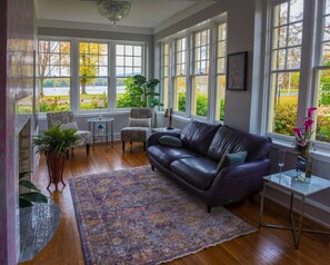A spacious room with a leather sofa, a patterned rug, and large windows offering a view of a garden.