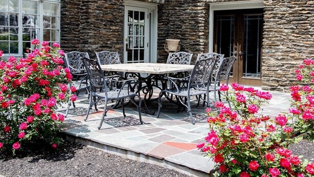 A stone building with a patio, a table with chairs, and pink flowers.