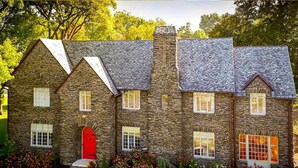 A stone house with a red door, multiple windows, and a chimney.