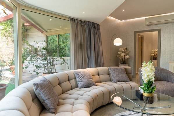 A modern living room with a curved sofa, a glass coffee table, and a view of a garden.