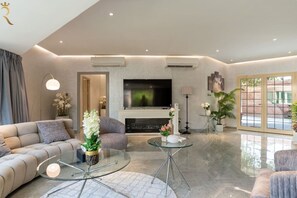 A modern living room with a sofa, two glass tables, a fireplace, and a TV.