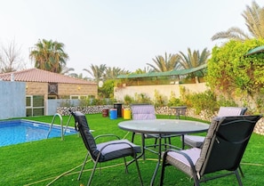 A backyard with a swimming pool, a round table, and chairs.