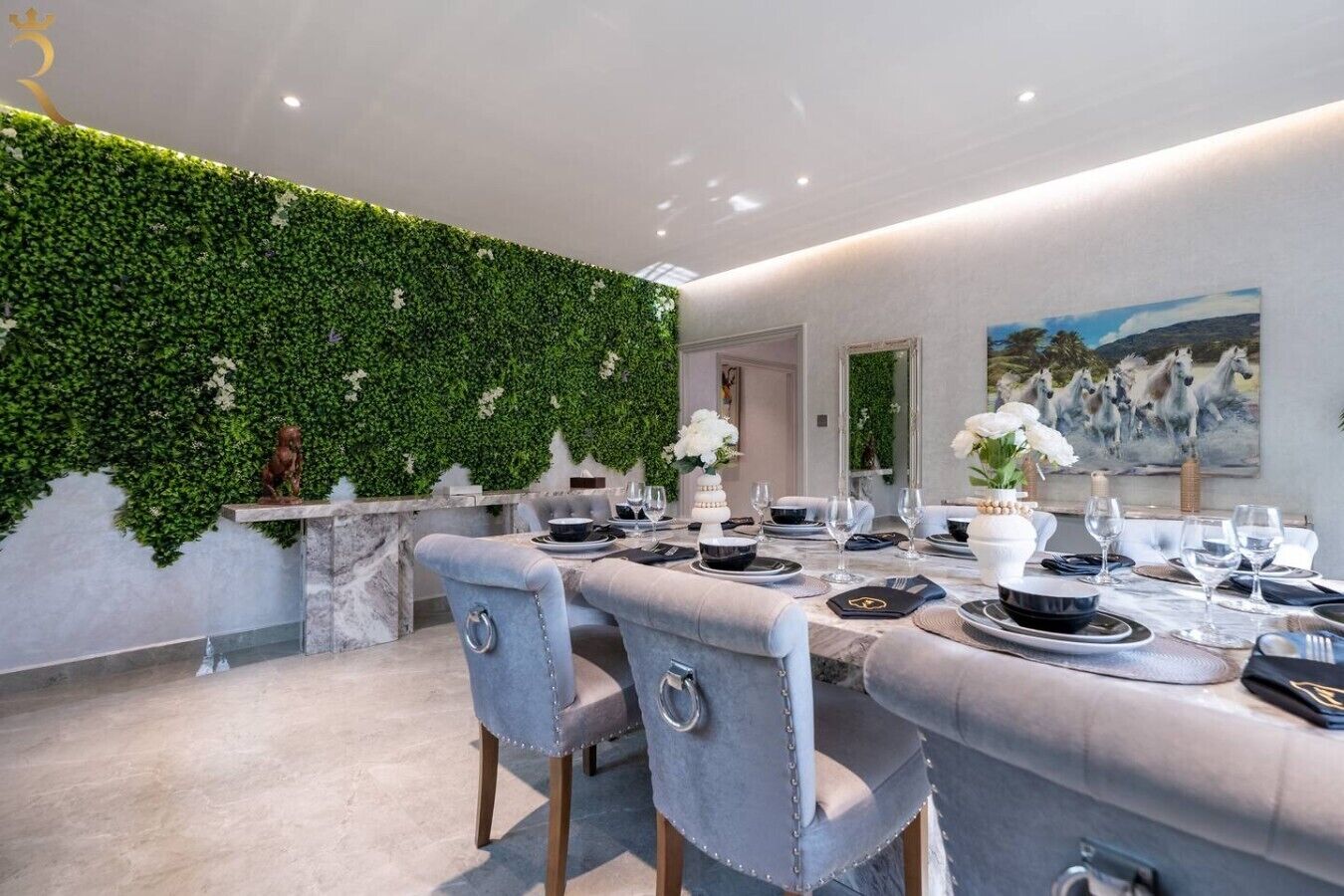 Un espace repas avec une longue table dressée pour le repas, un mur végétal et un tableau représentant des chevaux.