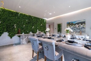A dining area with a long table set for a meal, a green wall with foliage, and a painting of horses on the wall.