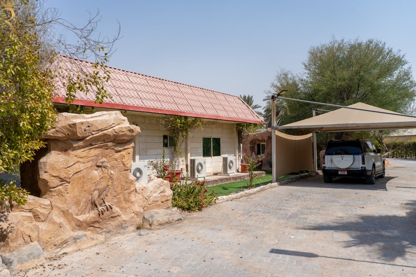 Ein Haus mit rotem Dach, ein Auto auf der Auffahrt und eine Felsformation links.