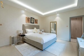 A modern bedroom with a large bed, bedside tables, a mirror, and artwork on the wall.