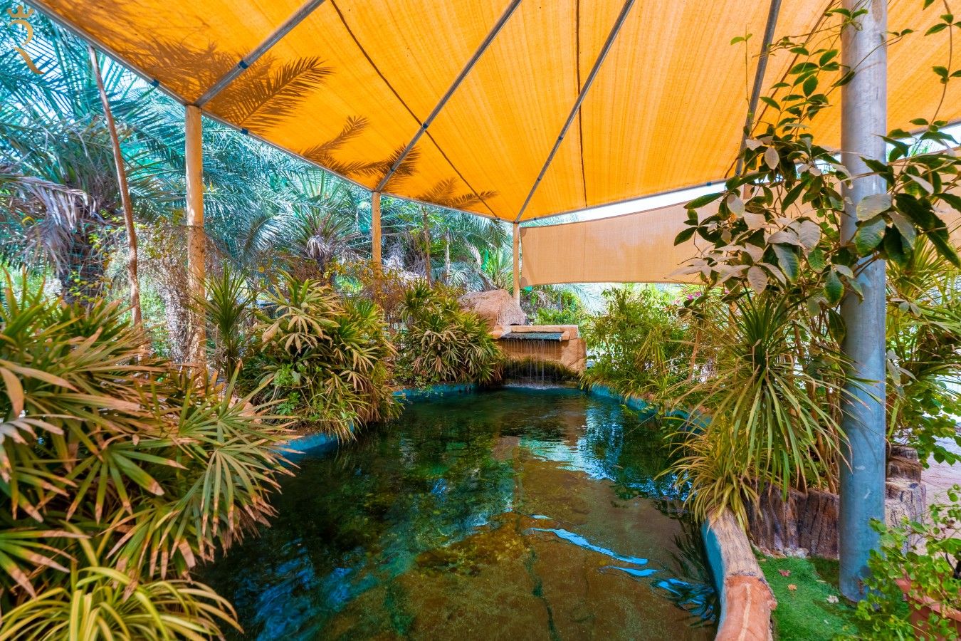 Un giardino interno con un elemento d'acqua, circondato da diverse piante e un tetto giallo.