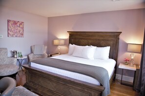 A hotel room with a large bed, two chairs, a small table with drinks, and a decorative vase. - The Schiaparelli Suite at The Manor on Front (Harrisburg)