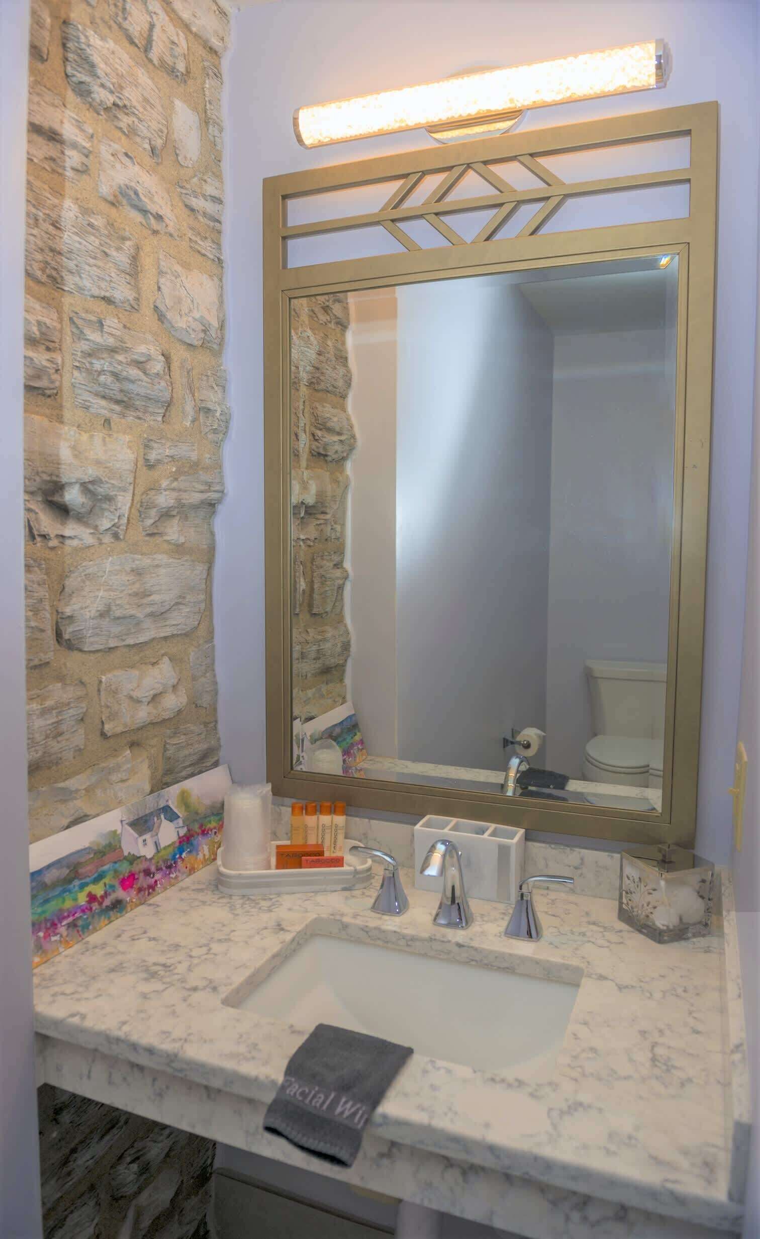 A bathroom with a stone wall, a marble sink, a large mirror, and a towel dispenser.
