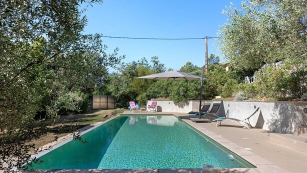 Piscina retangular com água cristalina, rodeada por um deck de concreto. Há espreguiçadeiras e um guarda-sol para dar sombra.