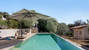 Piscina retangular com água cristalina, rodeada por um terraço com espreguiçadeiras e um guarda-sol.