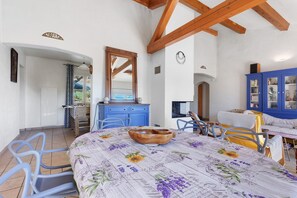 Une pièce avec un plafond en bois, une table à manger recouverte d’une nappe à motifs floraux et un buffet bleu.