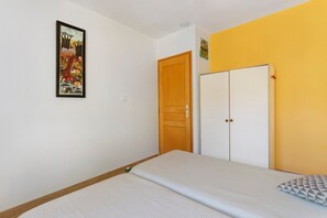 A bedroom with a single bed, a wooden door, a wardrobe, and a wall-mounted painting. - Holiday Home 'Les Loriots' with Private Pool, Wi-Fi, and Air Conditioning (Flassans-sur-Issole)