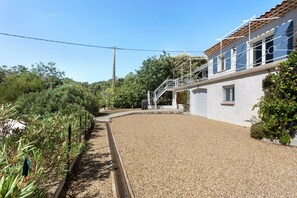 A residential property with a gravel driveway, a covered outdoor seating area, and a staircase leading to a second-floor balcony. - Holiday Home 'Les Loriots' with Private Pool, Wi-Fi, and Air Conditioning (Flassans-sur-Issole)