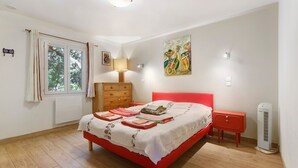 Quarto com cama vermelha, cómoda de madeira e radiador.