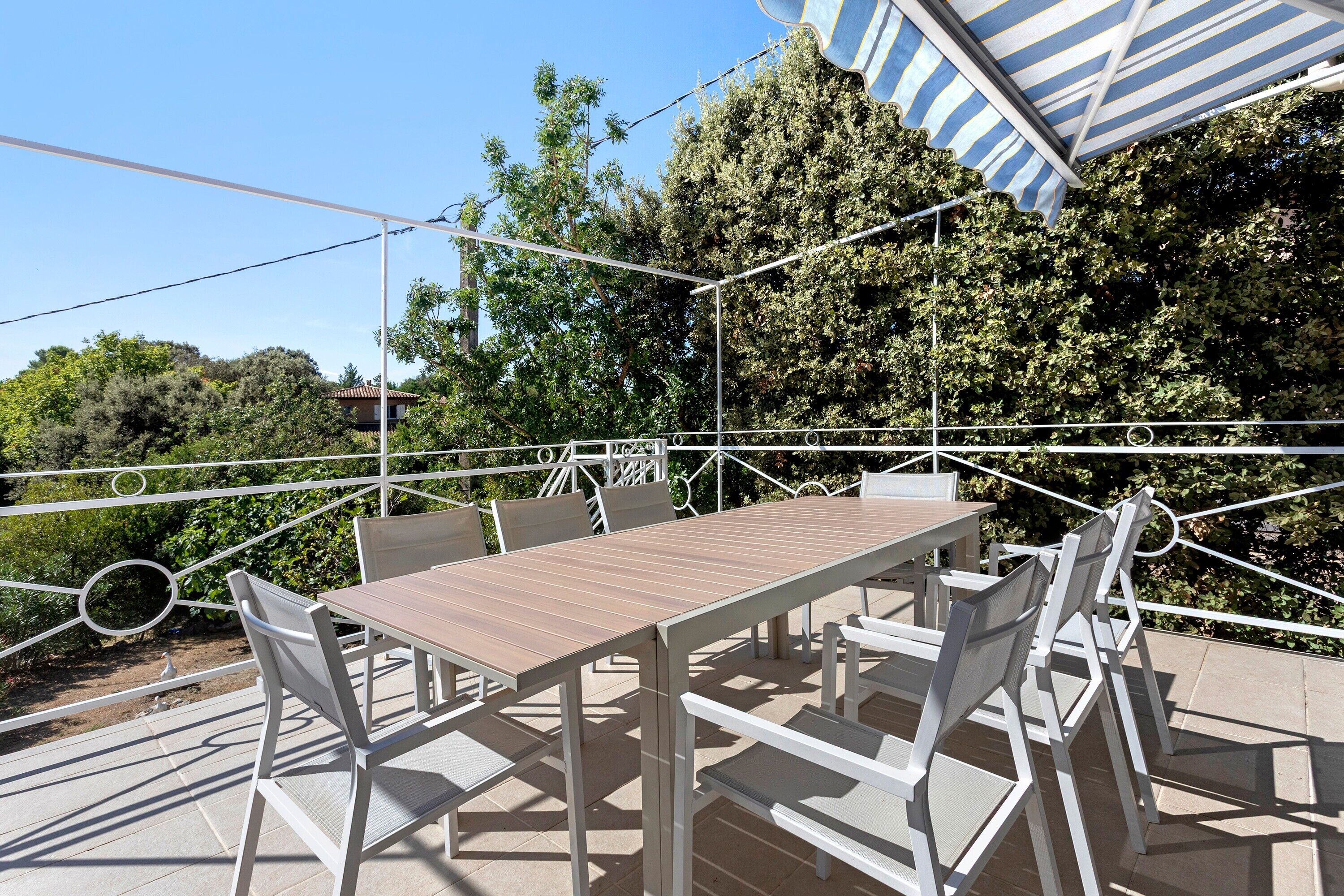 Une terrasse extérieure avec une table et des chaises, entourée d’une rambarde en métal blanc.