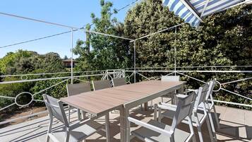 Une terrasse extérieure avec une table et des chaises, entourée d’une rambarde en métal blanc.