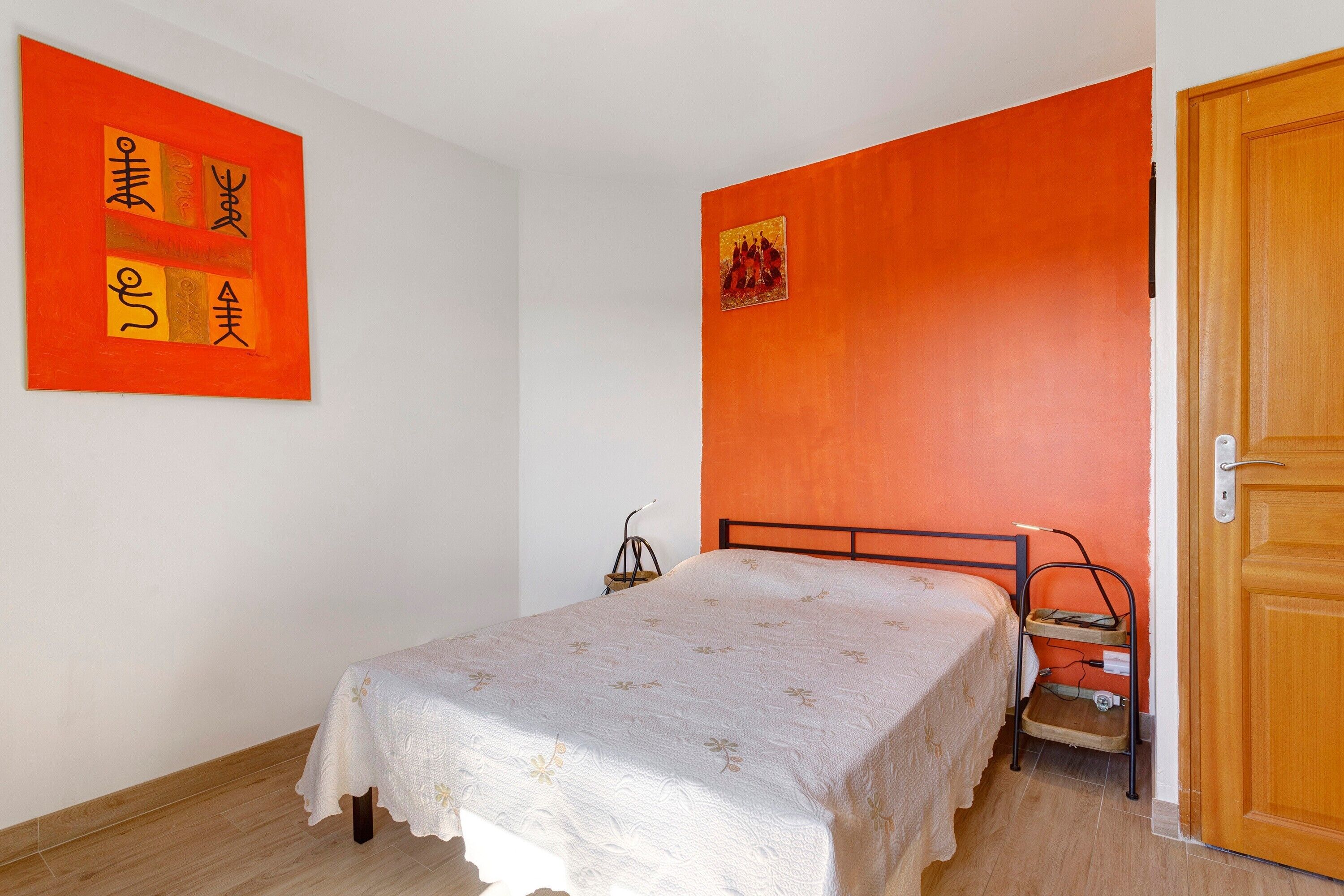 A bedroom with a bed, a wooden door, and a wall with a painting.