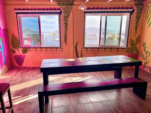 A room with a wooden floor, a black table with a colorful top, and two windows with decorative frames. - Private room boho, jacuzzi inside. Pool, roof (Cabo San Lucas)