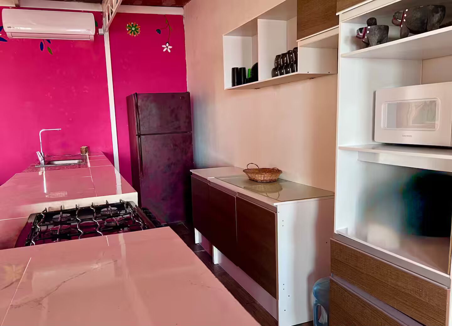 Eine kleine Küche mit einem Gaskochfeld, einem Kühlschrank und einer Mikrowelle auf einer weißen Arbeitsplatte.