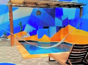 Ein Poolbereich mit Hängematte, Liegestühlen und einem geometrischen Wanddesign.