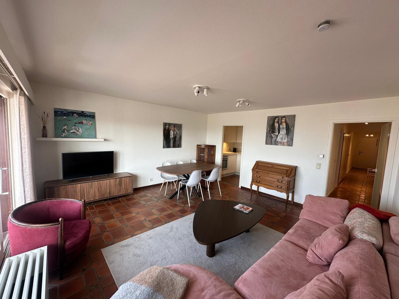 A living room with a television, a dining table with chairs, a sofa, and artwork on the walls.