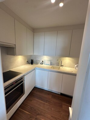 A compact kitchen with white cabinetry, a built-in oven, a sink, and a countertop. - MeDaMoRe - Beachfront (Knokke-Heist)