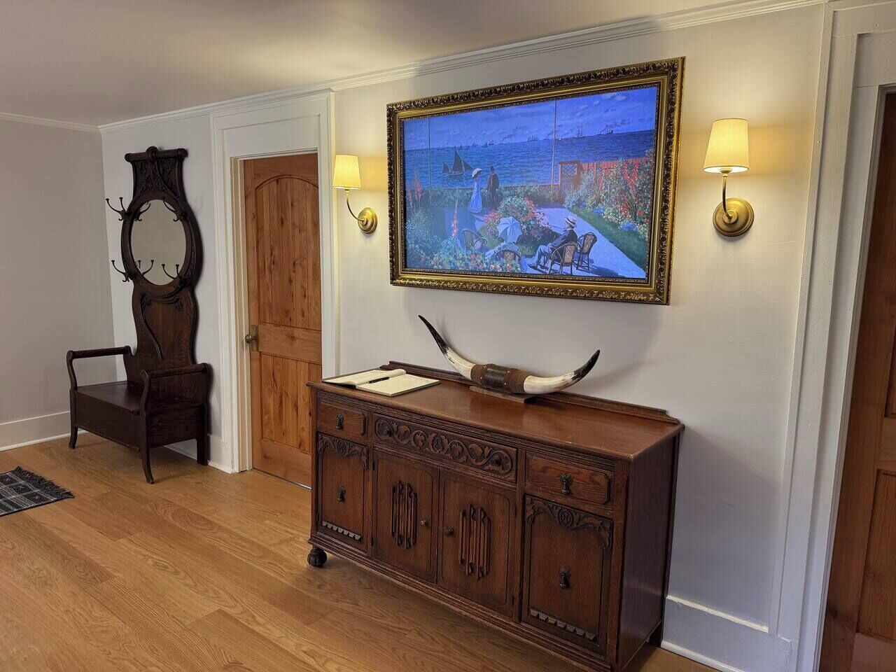 Un meuble en bois avec un tableau accroché au-dessus, un miroir au mur et une chaise dans le coin.