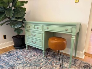 A light green desk with drawers and a bench, a potted plant, and a patterned rug. - Carriage House - Historic Louden Hay Trolley + EV (Fairfield)