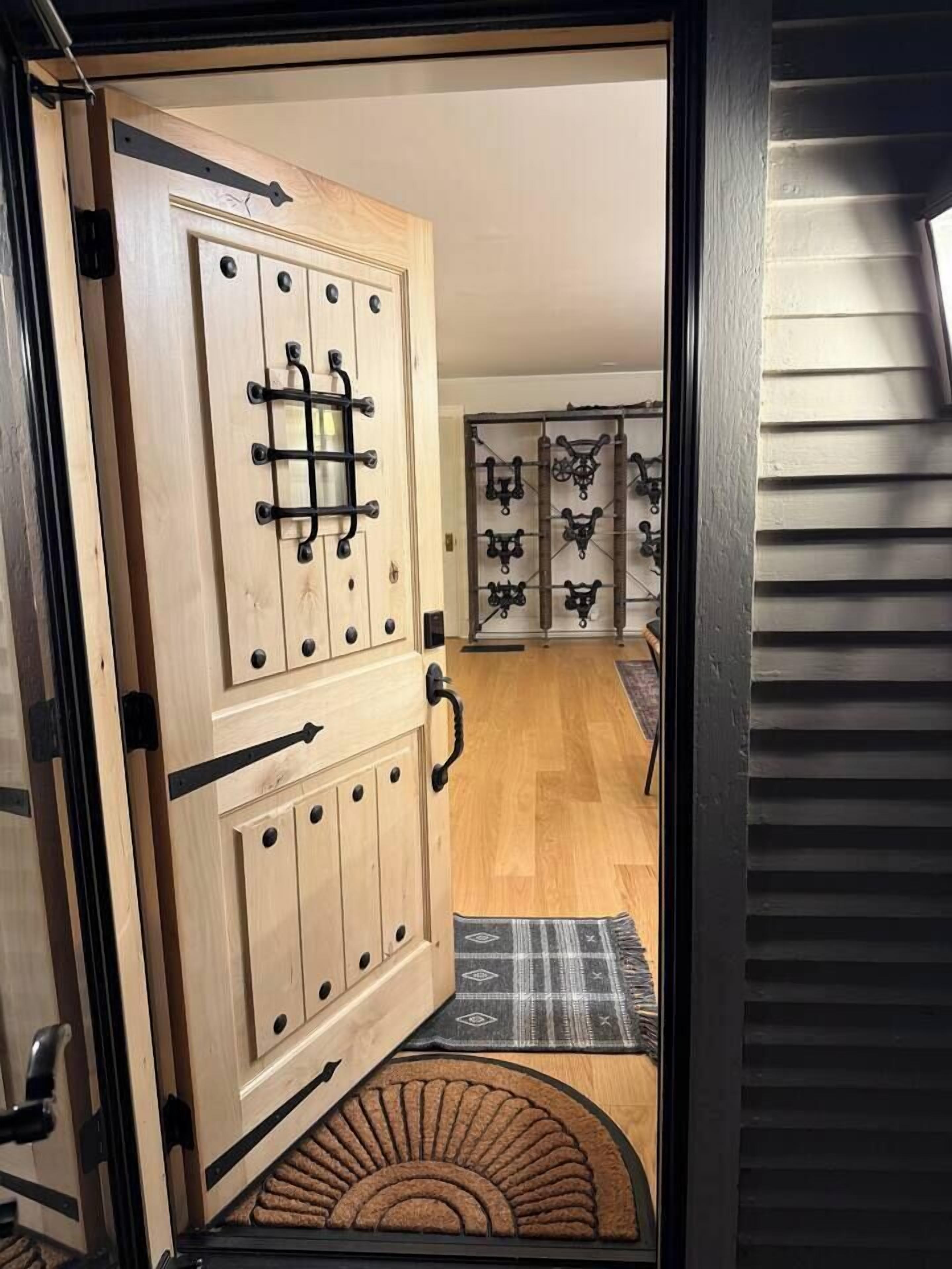 A wooden door with a black handle and a latch, leading to a room with a patterned rug and a small rug at the entrance.