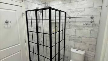 A bathroom with a glass-enclosed shower, a toilet, and tiled walls.