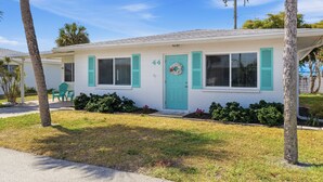 A single-story house with a light-colored exterior, numbered 44, featuring a front porch with a green door and shutters, and a small front yard with grass and shrubs. - Paradise on Pearl 2-bedroom bungalow at Englewood Beach (Englewood)