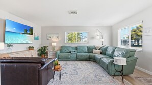 A living room with a sectional sofa, a brown leather couch, a patterned rug, and artwork on the walls. - Paradise on Pearl 2-bedroom bungalow at Englewood Beach (Englewood)