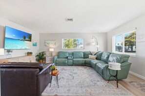 A living room with a sectional sofa, a brown leather couch, a patterned rug, and artwork on the walls. - Paradise on Pearl 2-bedroom bungalow at Englewood Beach (Englewood)