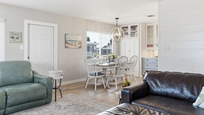 A modern living room with a leather sofa, a dining area with white chairs, and a kitchen with white cabinets. - Paradise on Pearl 2-bedroom bungalow at Englewood Beach (Englewood)