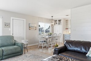 A modern living room with a leather sofa, a dining area with white chairs, and a kitchen with white cabinets. - Paradise on Pearl 2-bedroom bungalow at Englewood Beach (Englewood)