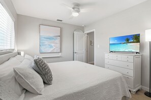 A bedroom with a bed, a TV on a dresser, and a painting on the wall. - Paradise on Pearl 2-bedroom bungalow at Englewood Beach (Englewood)