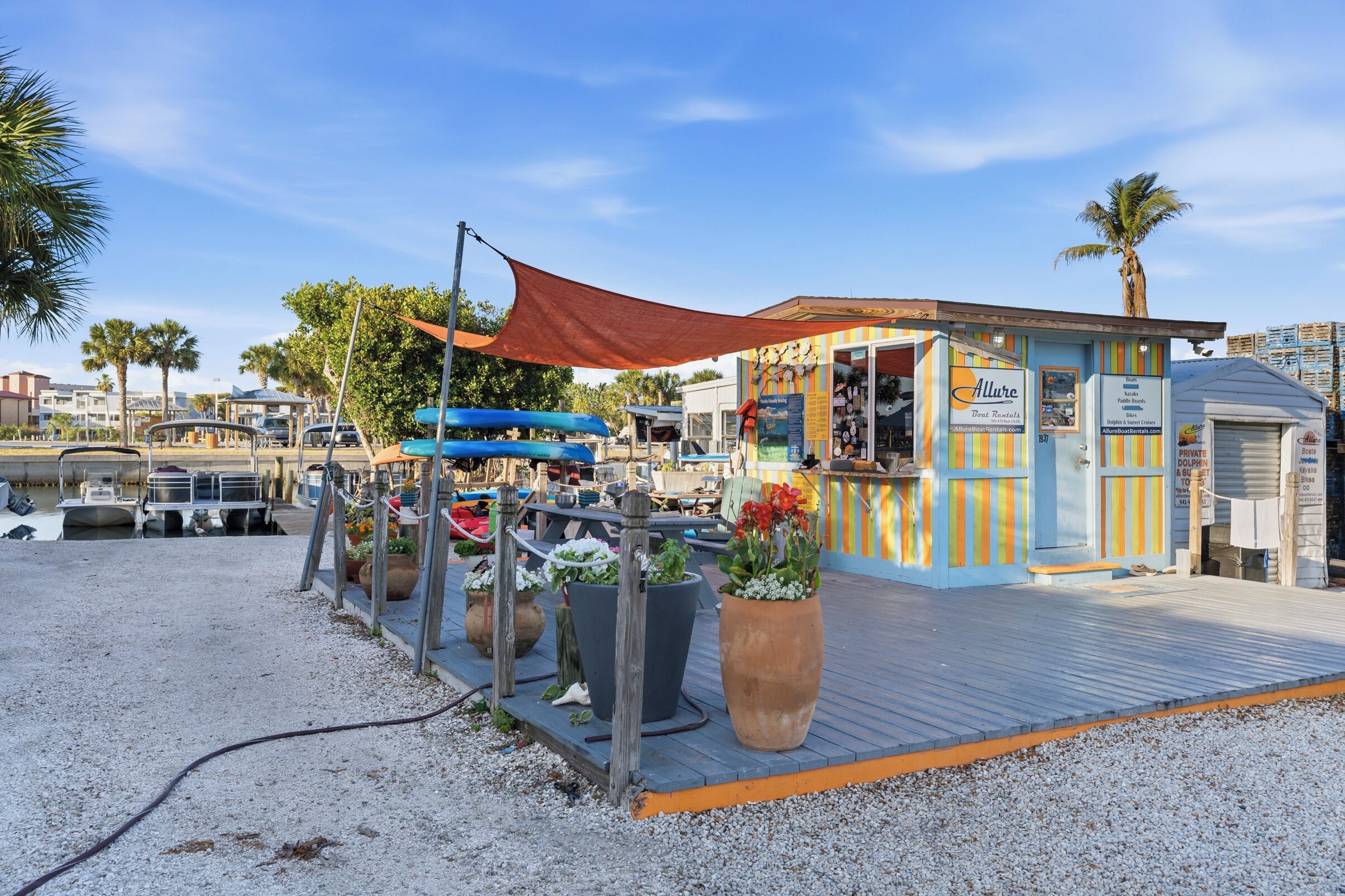 A waterfront restaurant with outdoor seating, a boat rental sign, and a small building with colorful vertical stripes.