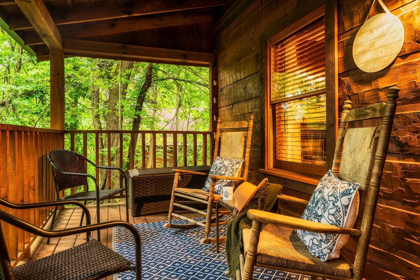 Een houten veranda met rieten stoelen en een patroon vloer, uitkijkend op een bebost gebied.
