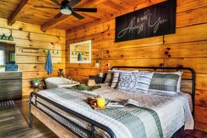 A wooden cabin bedroom with a bed, bedside table, and a ceiling fan. - Romantic - Firepit - Hot tub - Pet Friendly (Sevierville)