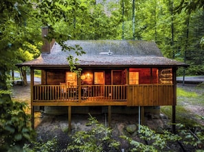 A wooden cabin with a deck, surrounded by trees. - Romantic - Firepit - Hot tub - Pet Friendly (Sevierville)