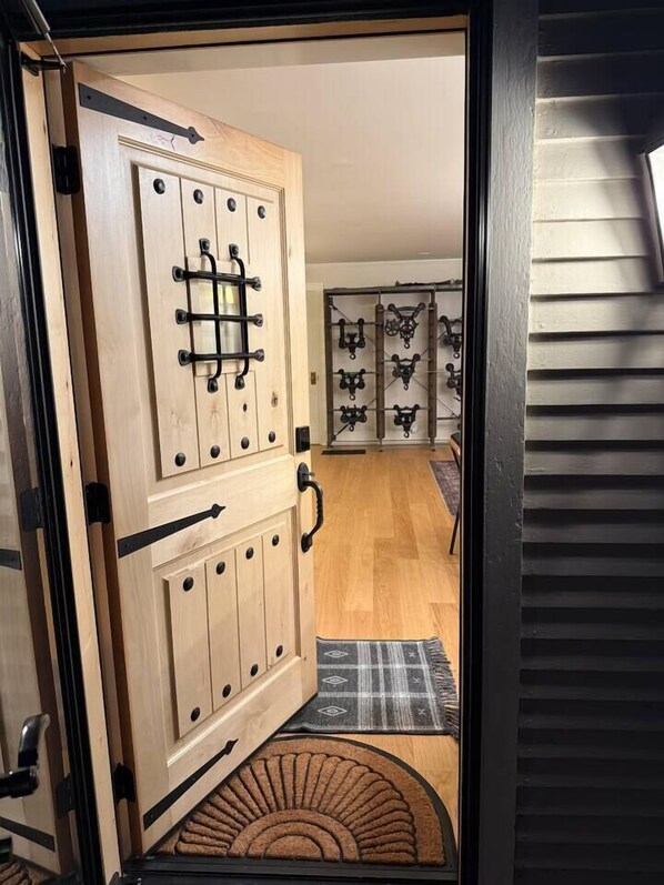 A wooden door with a metal handle and a small window, leading to a room with a patterned rug and a curved mat.